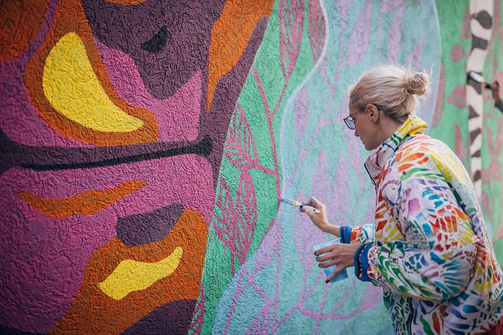 kobieta malująca mural na ścianie budynku